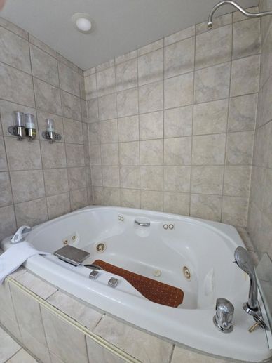 A clean white jacuzzi tub with beige tiled walls and mounted soap dispensers.