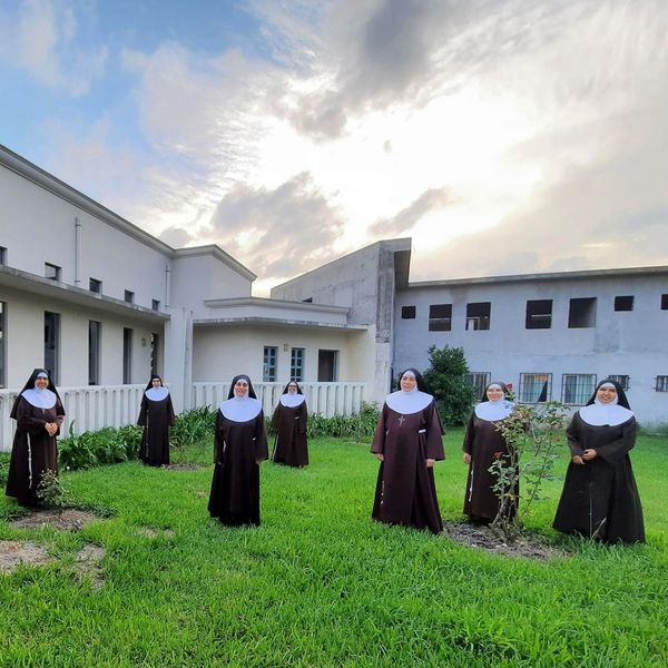 A group of nuns standing spaced apart on a grassy lawn near buildings.