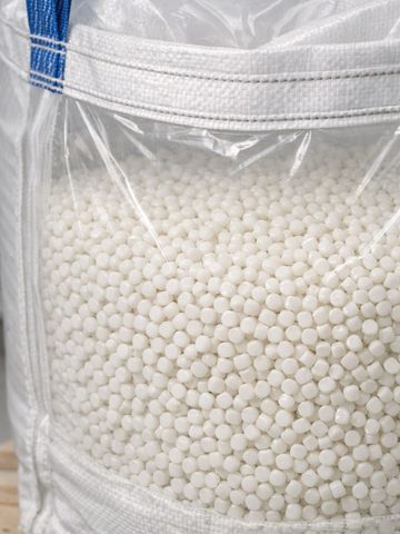 Large bag filled with small white plastic pellets on a wooden pallet.