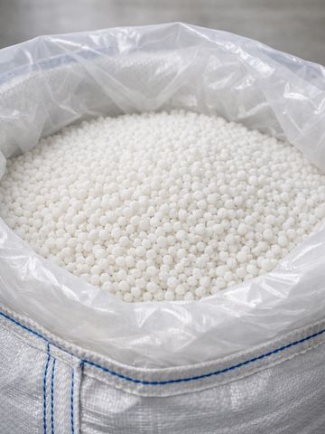 Large white sack filled with small white pellets, lined with plastic.