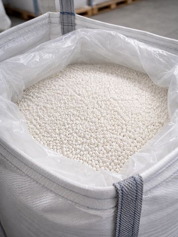 Large white industrial bag filled with small white pellets in a warehouse.