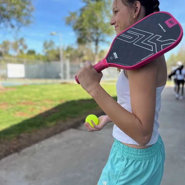 A woman holding a pickleball paddle and ball outdoors.