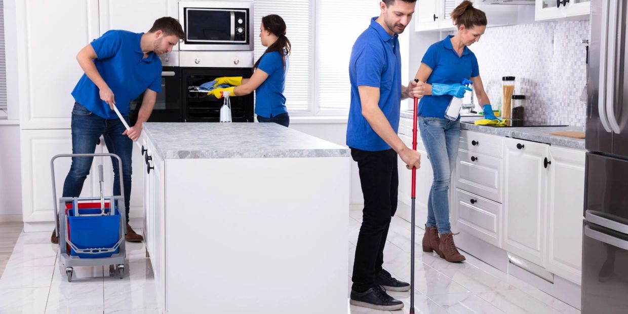 Four people in blue shirts cleaning a modern white kitchen together.