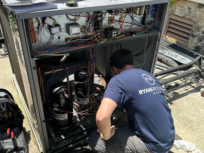 Technician repairing an open HVAC unit outdoors.