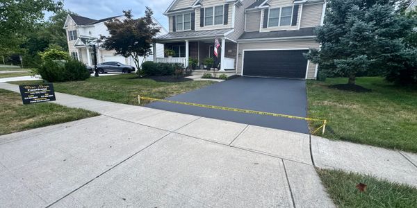 Freshly paved driveway with caution tape in front of a two-story house.