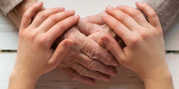Young hands gently holding elderly hands, symbolizing care and support.