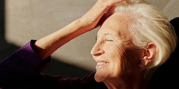 Elderly woman smiling with eyes closed, basking in warm sunlight.
