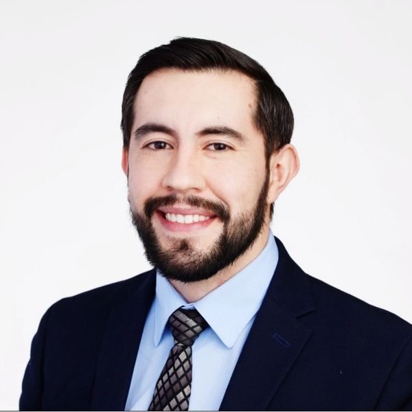Professional young man in suit smiling against a white background.