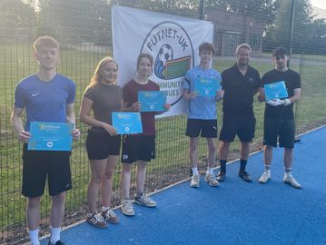 Group of six holding certificates on a sports field.