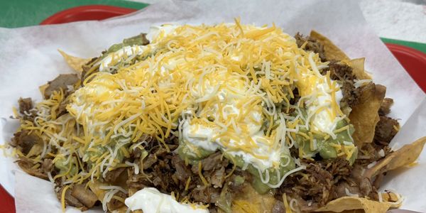 A plate of nachos topped with shredded beef, guacamole, sour cream