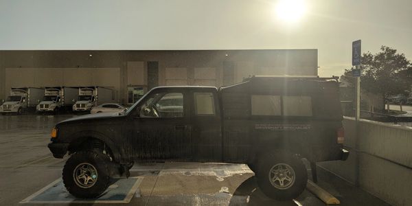 Black lifted truck parked in a handicapped spot at sunset with wet ground.