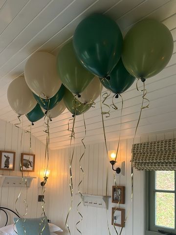 Green and cream balloons hang from the ceiling in a cozy room.