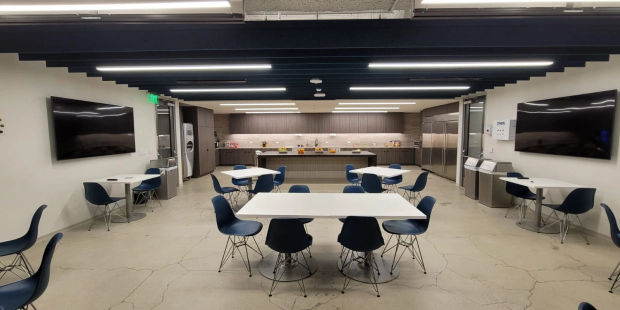 Modern office kitchen and dining area with tables and chairs.