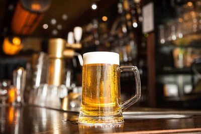 A cold beer sitting on a wooden bar.