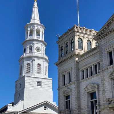Historic white church steeple and stone building with American flag against clear blue sky.