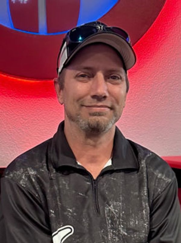 Man smiling wearing a cap and sunglasses indoors.