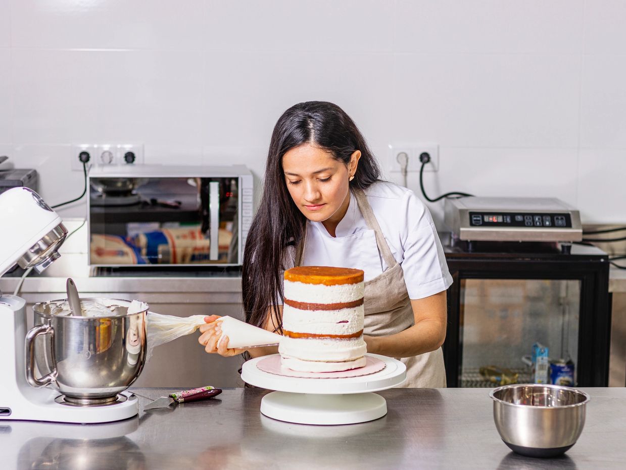Baker applying frosting on a cake in a professional kitchen.