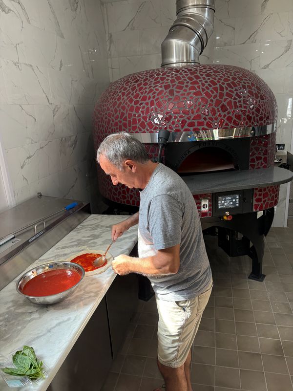 The Angelo saucing a pizza using San Marzano tomatoes imported from Italy