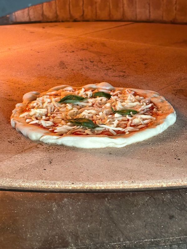 Margherita pizza featuring fresh mozzarella, basil and marinara in our imported Manna Forni oven