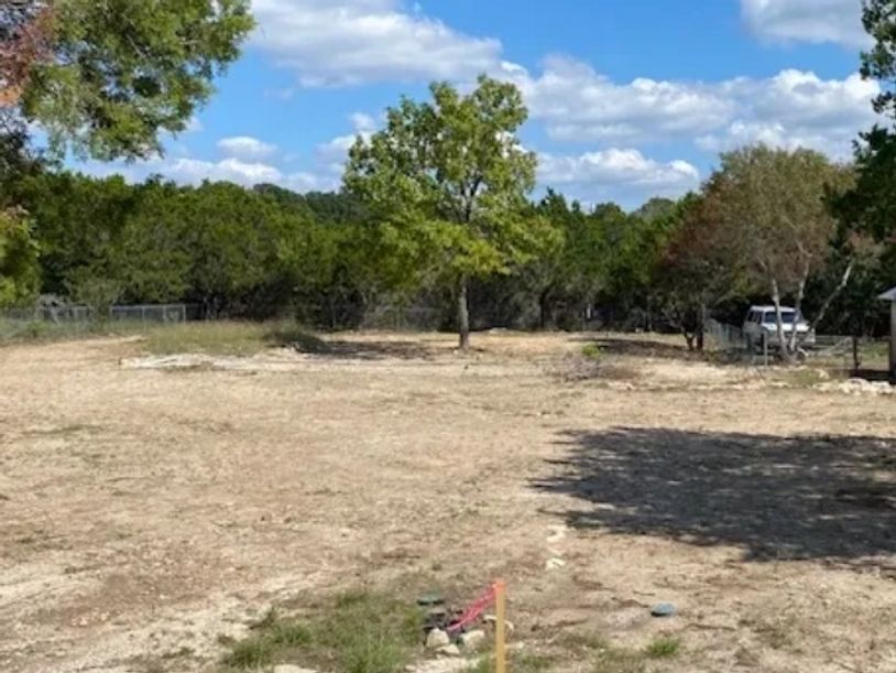 Open dry land with scattered trees and a partly cloudy sky.
