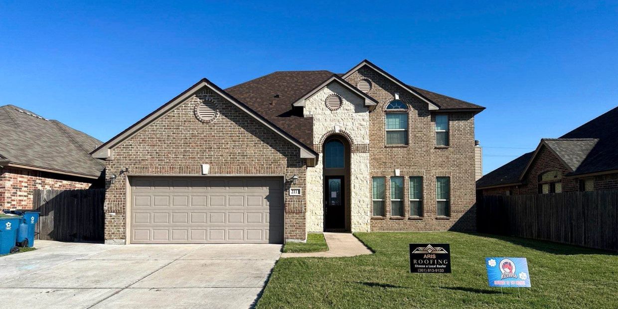 A two-story brick house with a front lawn and roofing signs.