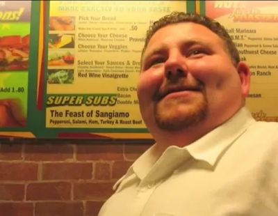 Smiling man sitting in a restaurant with a menu behind him.