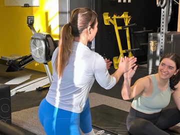 Two women in workout clothes high-five in a gym setting.