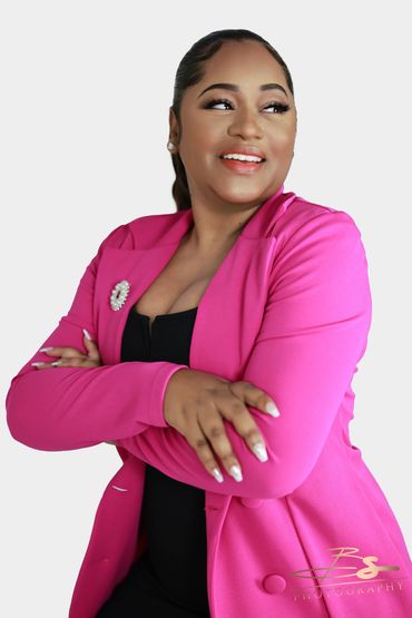 Confident woman in a vibrant pink blazer smiling with arms crossed.