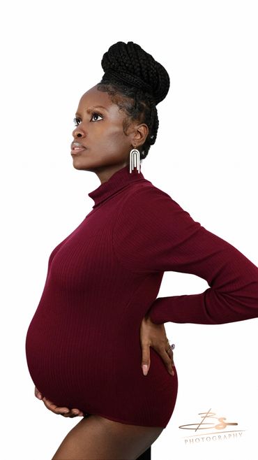 Pregnant woman in burgundy turtleneck posing in profile with hand on back.