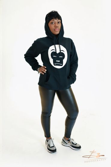 Woman wearing a black hoodie with a white gorilla face print and black leather pants.