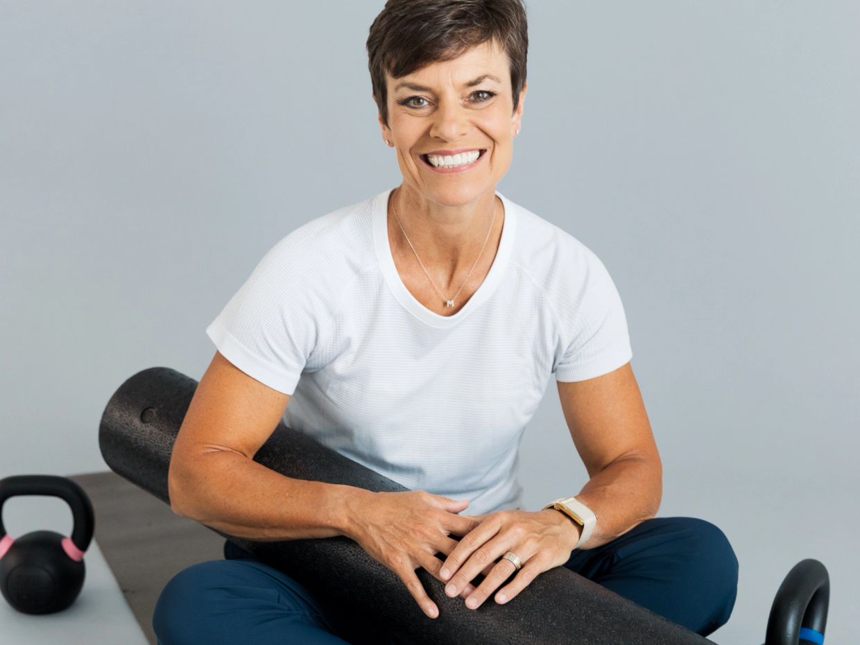 Woman smiling with foam roller and kettlebells.