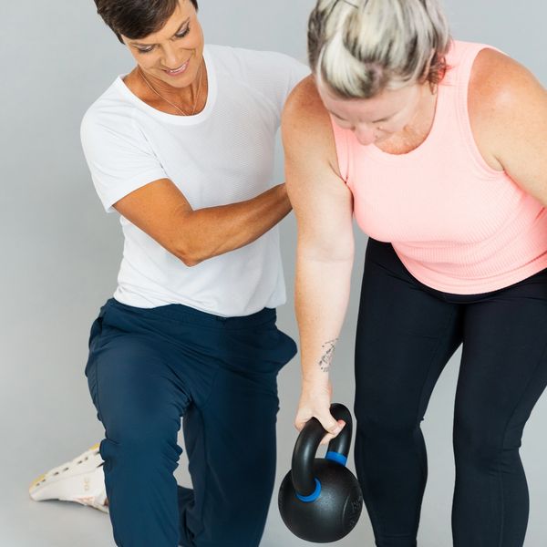 Personal trainer guiding a woman with kettlebell exercise.