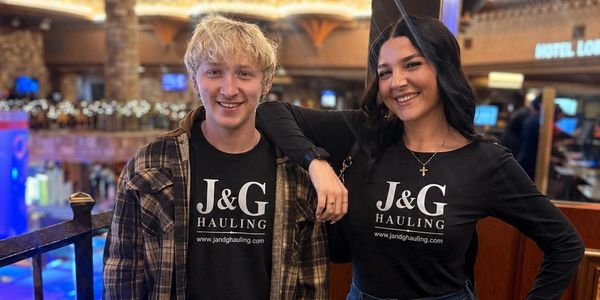 Two people wearing matching J&amp;G Hauling shirts smiling indoors.