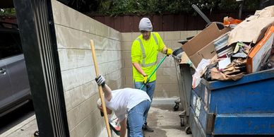 Two workers cleaning up near a dumpster.