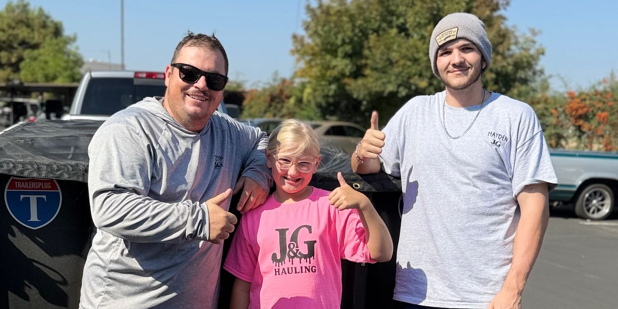 Three people posing with thumbs up outdoors in casual clothes.