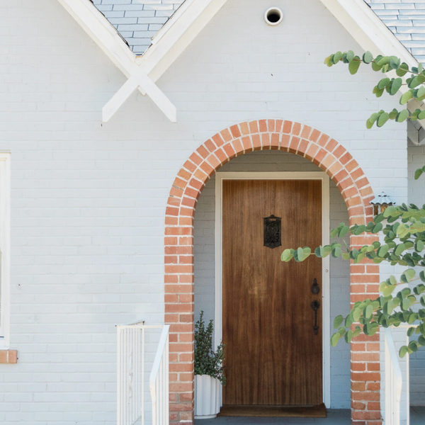 Beautiful dove colored brick home with contrasting copper toned brick trim framed by tree leaves.