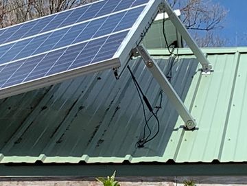 Close-up of solar panel mounted on a green metal roof under clear sky.