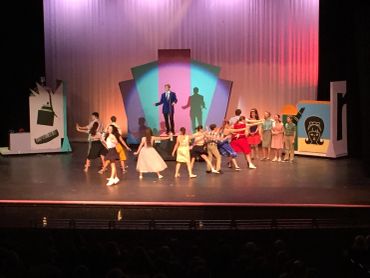 Group dance performance on stage with colorful backdrop.