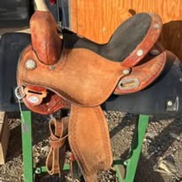 A worn brown leather horse saddle on a stand outdoors.