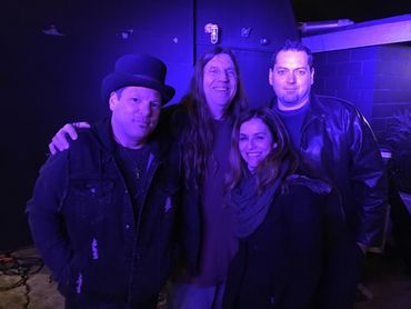 Four people posing together under purple lighting in a casual setting.