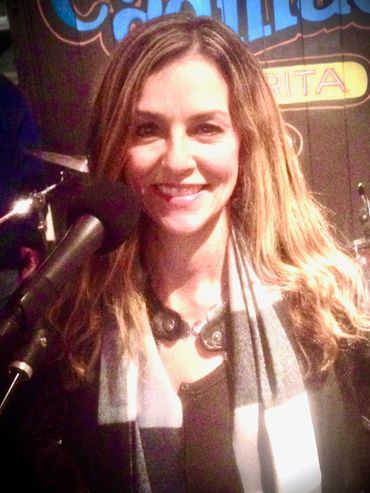 A woman smiling behind a microphone at a casual event.