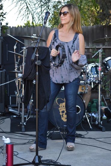 Woman singing and playing tambourine on outdoor stage.