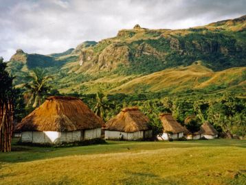 Thatched houses at the base of a green mountain.