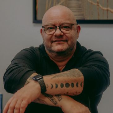 Bald man with glasses and tattooed arms smiling.