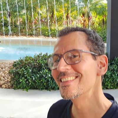 Man smiling near a fountain and greenery.