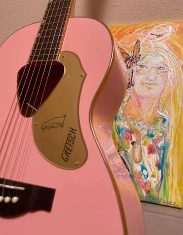 Pink Gretsch guitar with a colorful painting in the background.