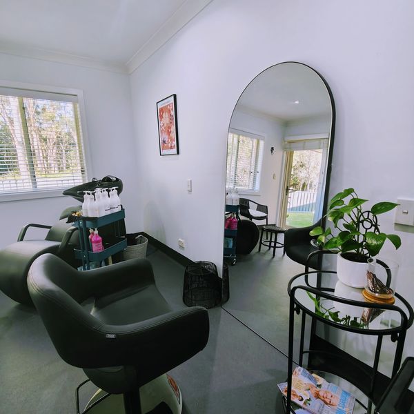 Single salon chair facing arched mirror with washing basin in background at home hair salon