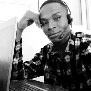 Man wearing a headset working on a laptop and looking at the camera.