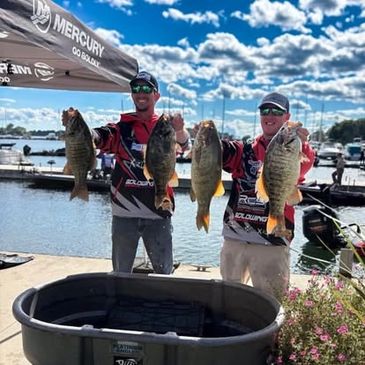 Two fishermen proudly display their large catches by the water.