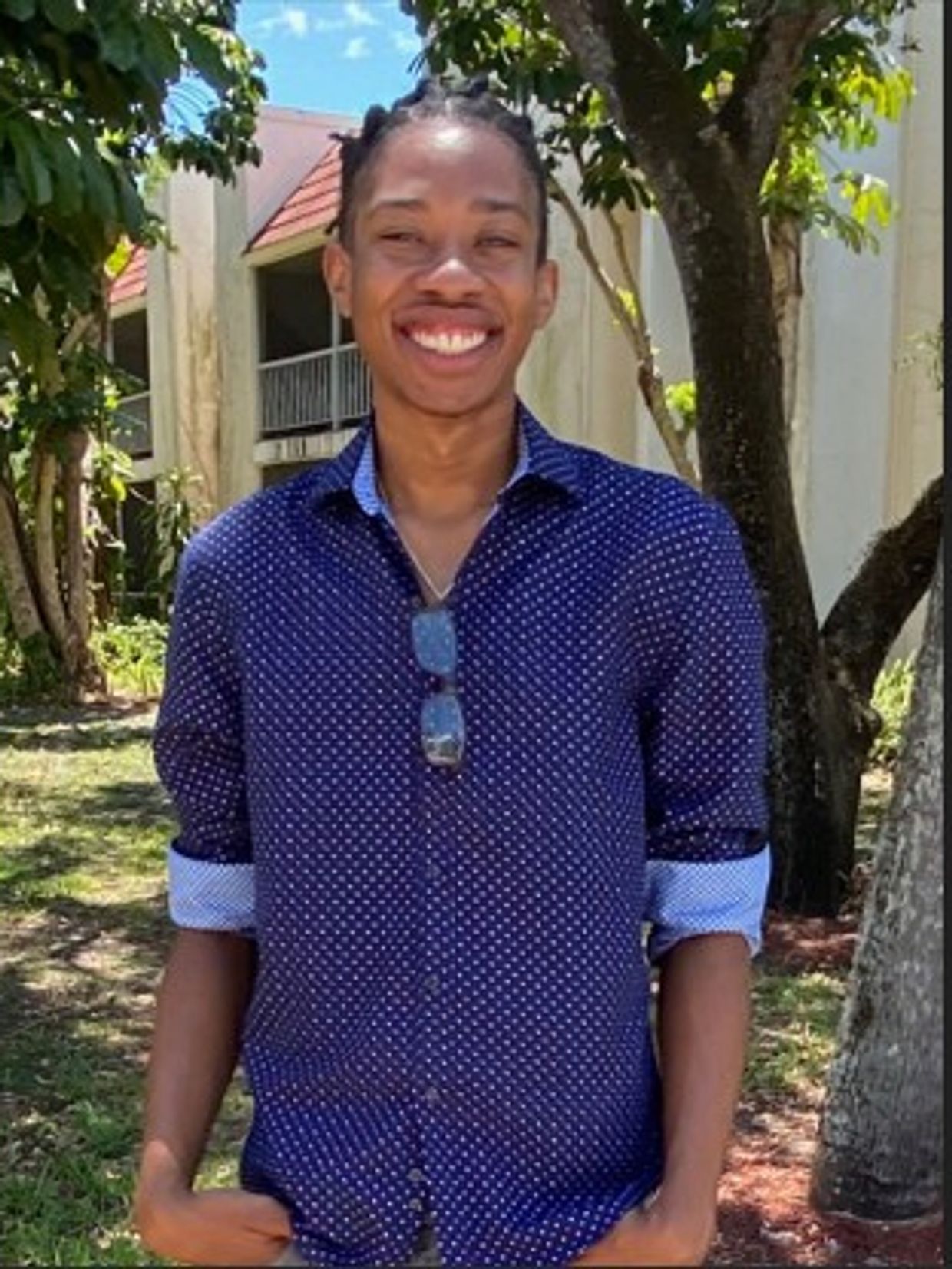 Smiling young man in a blue polka dot shirt outdoors.